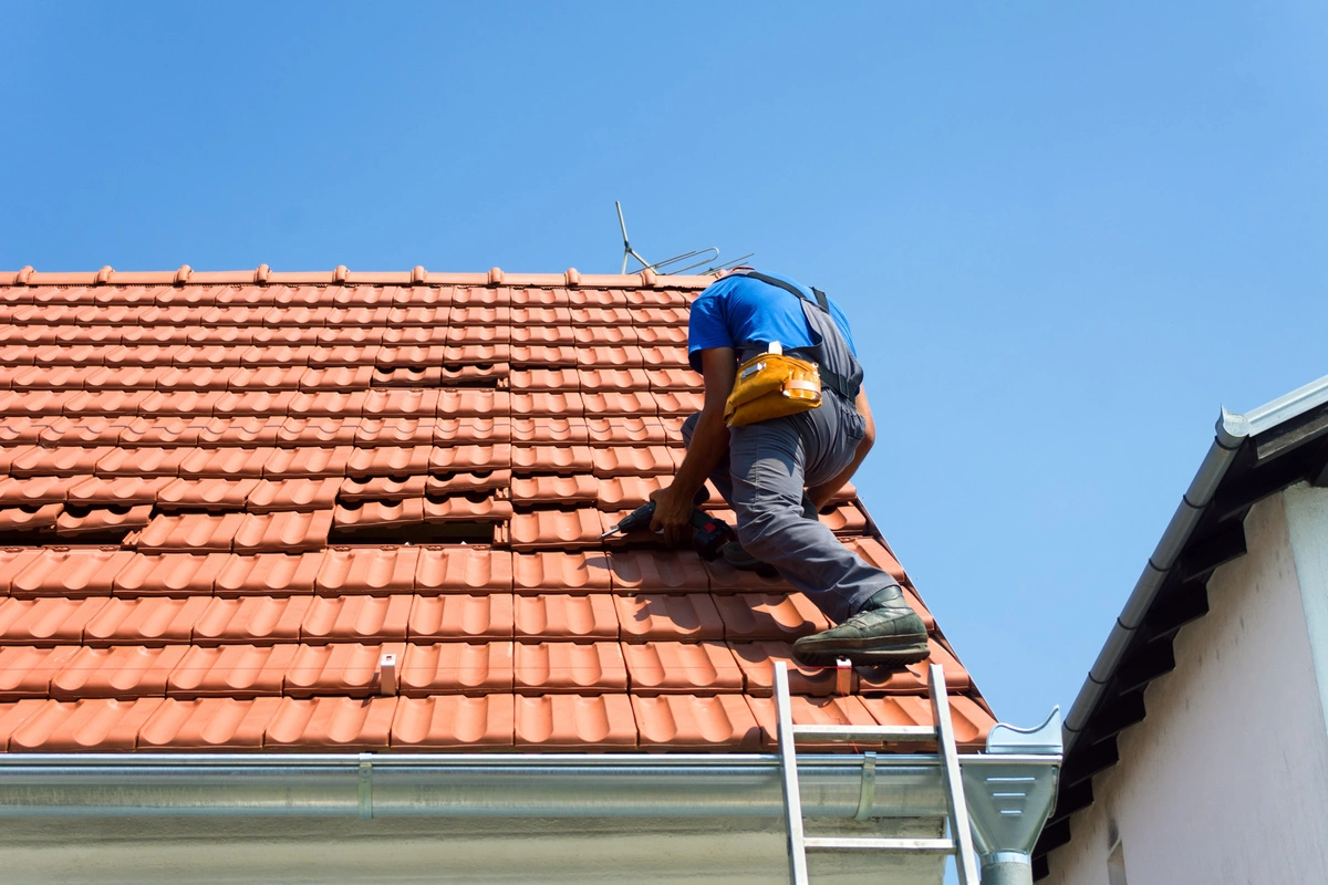 Couvreur effectuant des travaux de réparation sur une toiture en tuiles.
